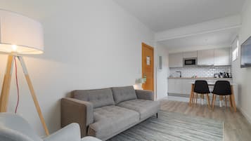 A modern living room with a grey sofa, a lamp, and a dining area with two chairs and a table.