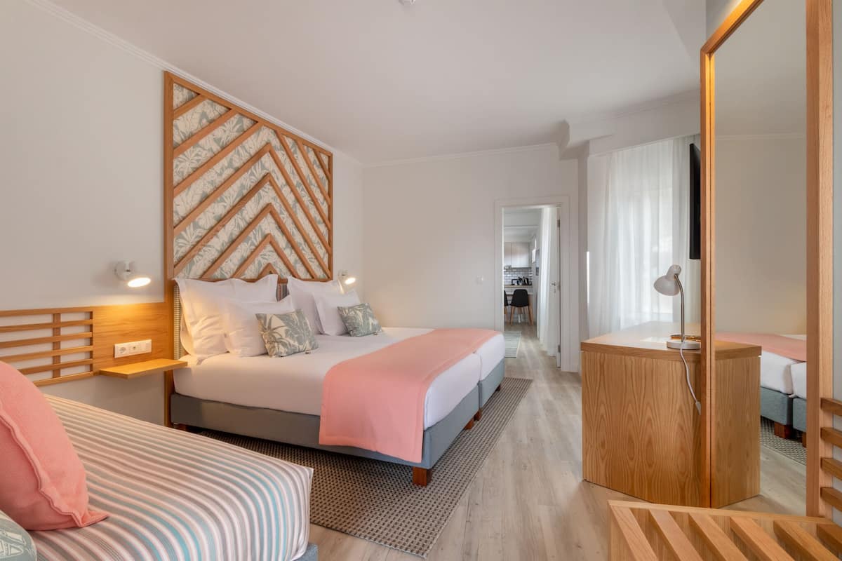 Una habitación de hotel moderna con una cama grande, una mesita de noche, un cabecero de madera y un pequeño escritorio con una silla.