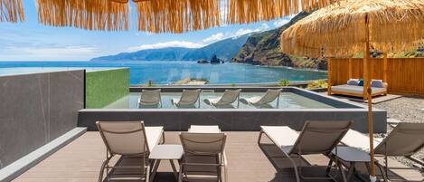 A poolside area with lounge chairs, a thatched umbrella, and a view of the sea.