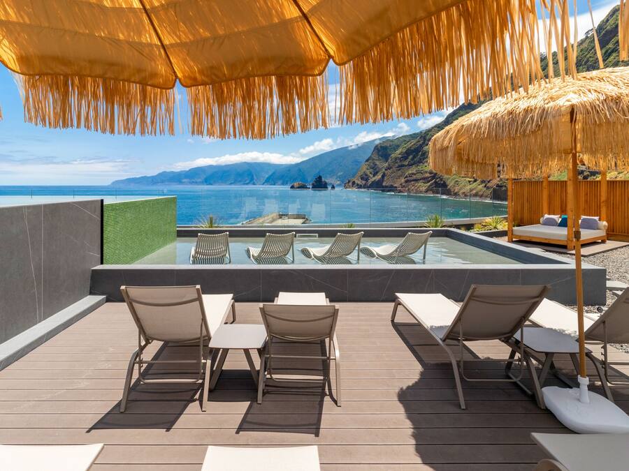 A poolside area with lounge chairs, a thatched umbrella, and a view of the sea.