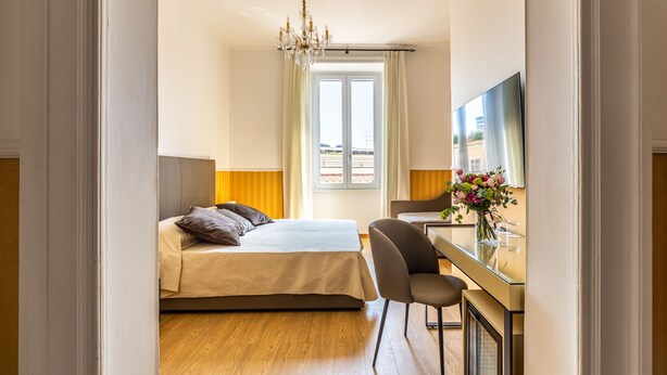 Una habitación de hotel con cama, escritorio, silla, televisor y ventana con cortinas.