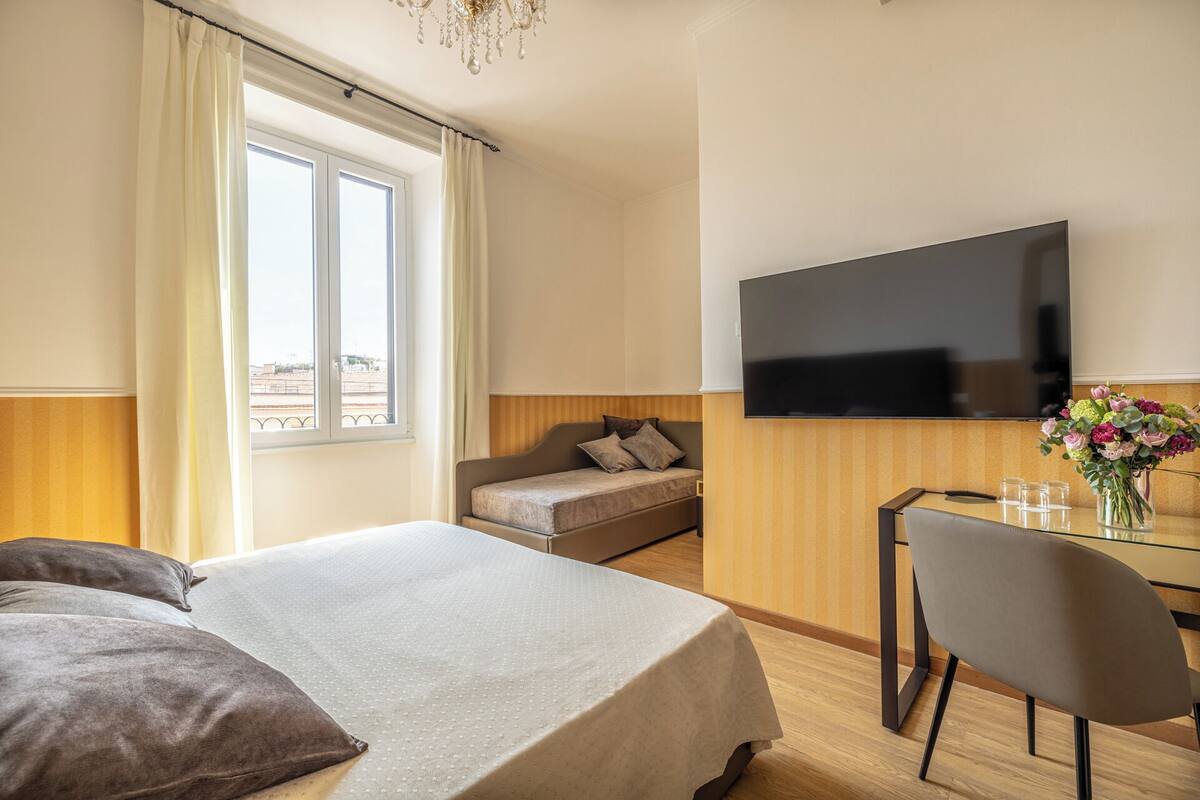 Una camera d'albergo con un letto, un divano, una televisione e un tavolo da pranzo con sedie.