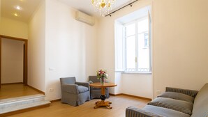 Un salón con piso de madera, sofás a rayas, una mesita redonda con un florero y una ventana con vistas.