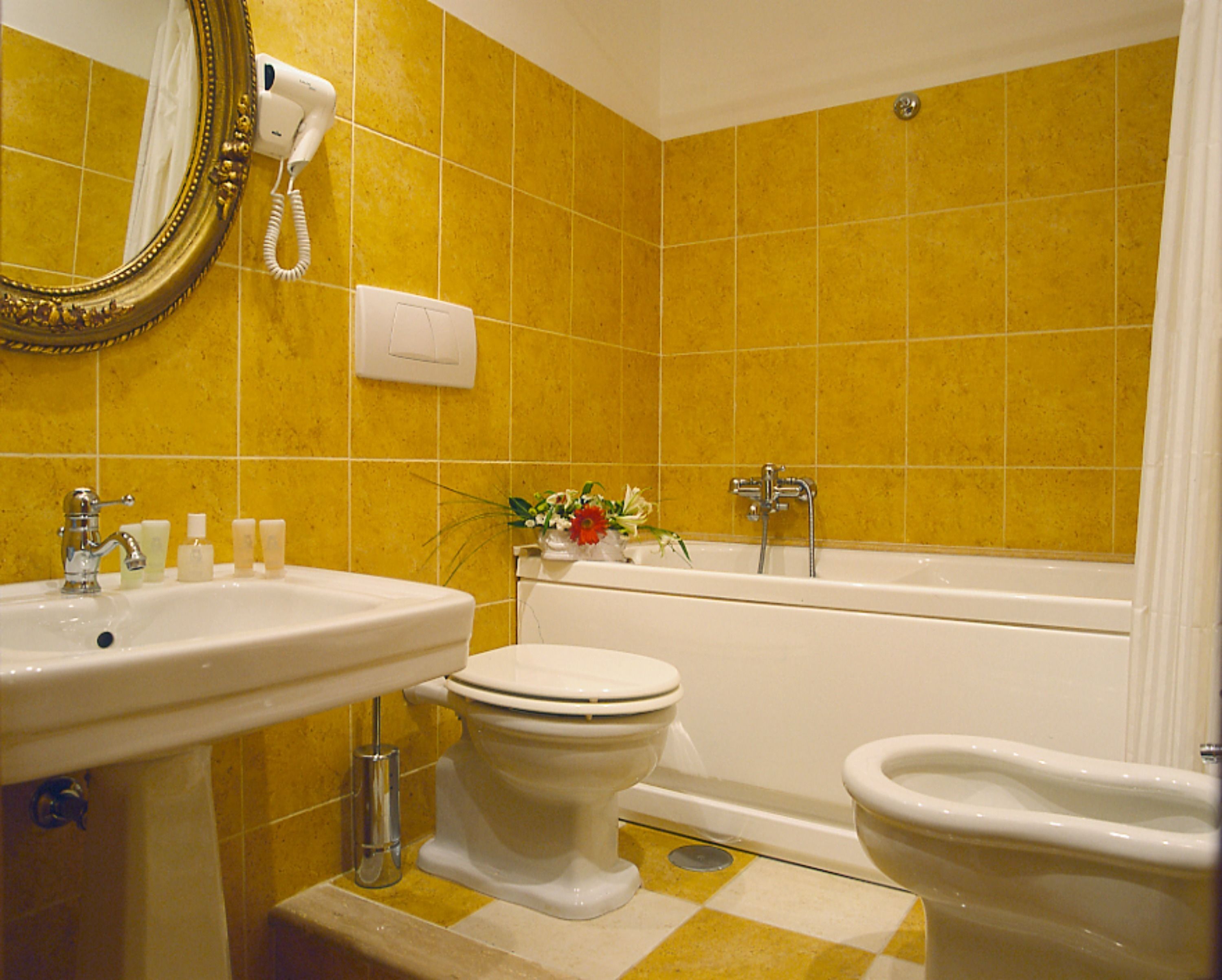A bathroom with yellow tiles, a white sink, a toilet, a bidet, and a bathtub.