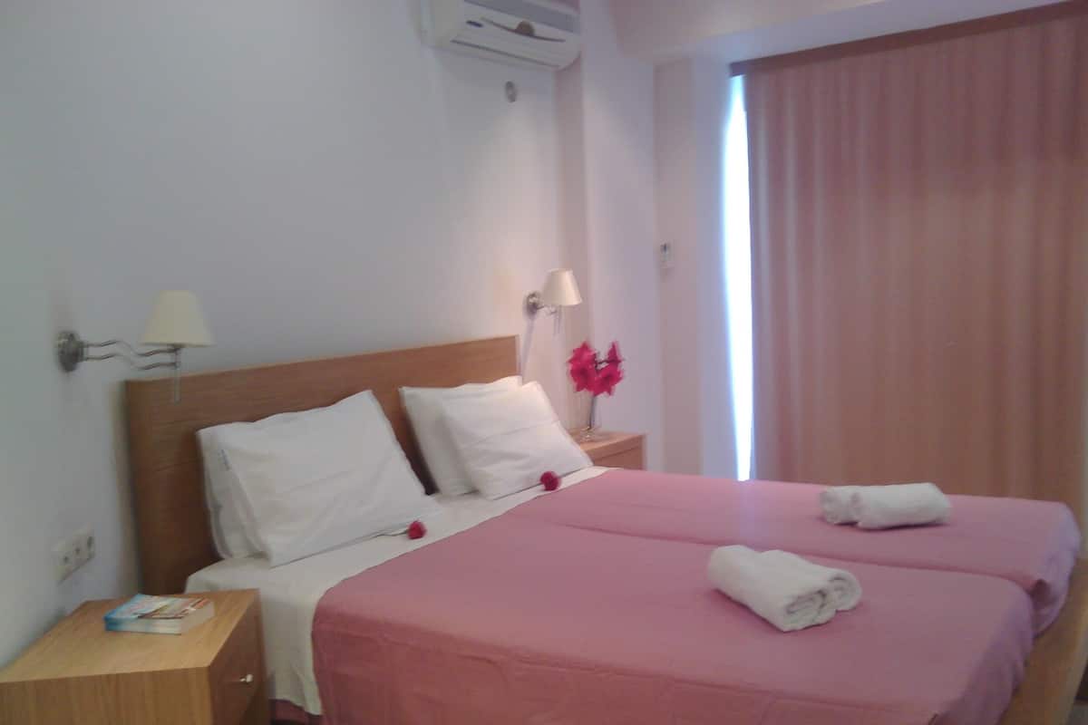 A double bed with pink bedding, white pillows, and two white towels on the bed.