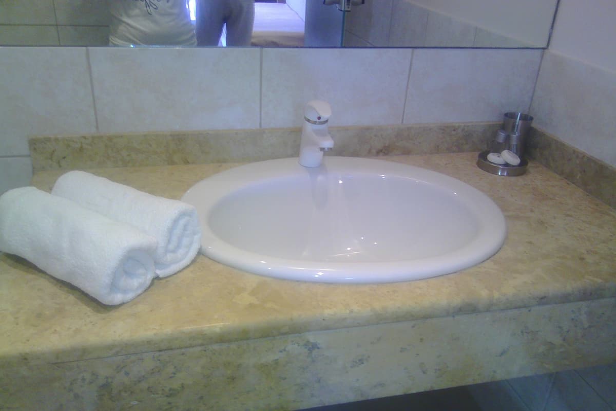 A bathroom with a white sink, two rolled towels, and a mirror above the sink.