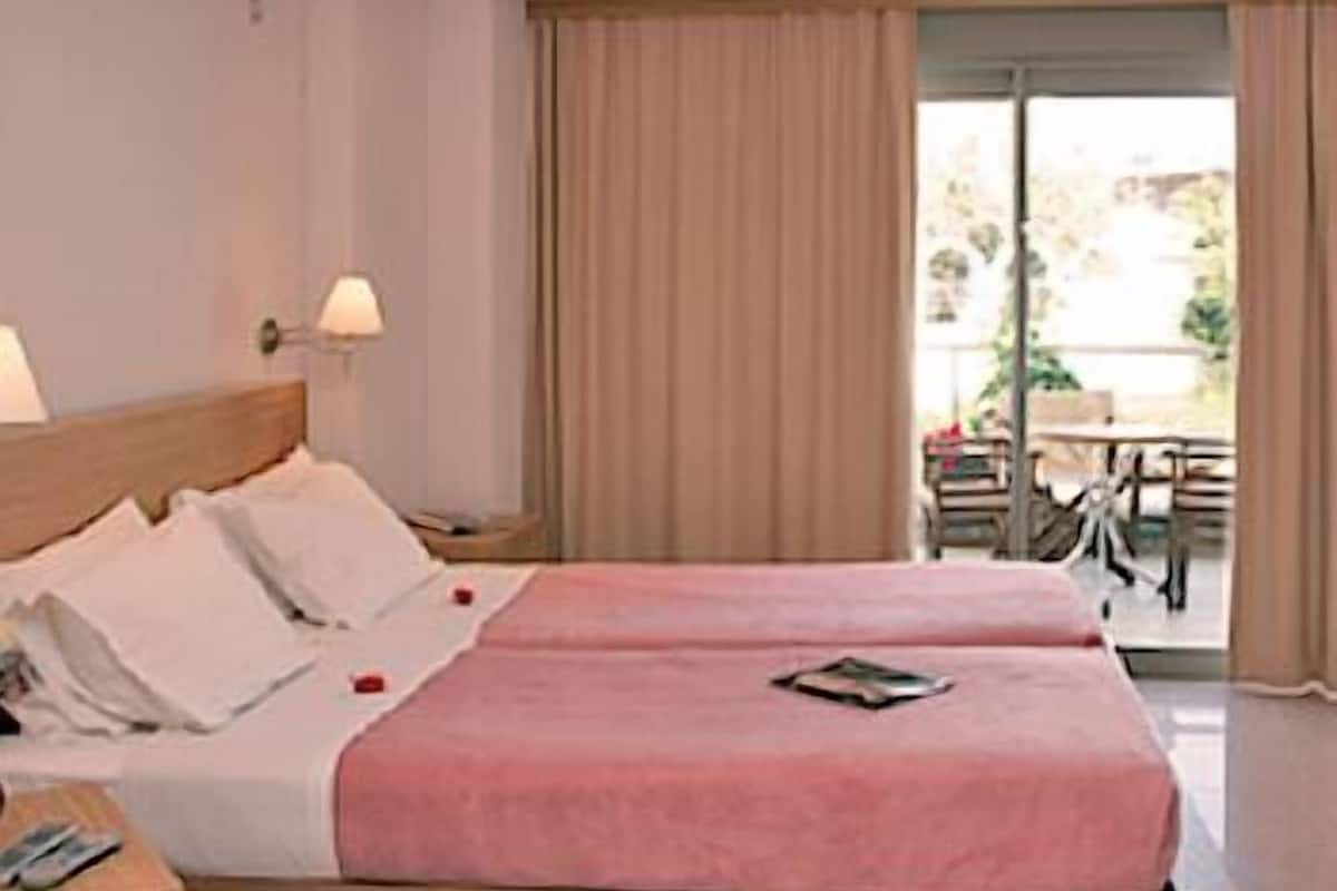 A hotel room with a double bed, a bedside table, a lamp, and a view of an outdoor area with a table and chairs.