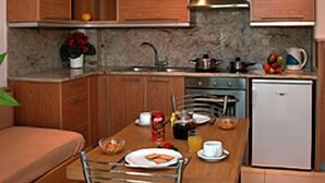 A compact kitchen with wooden cabinets, a built-in oven, and a small refrigerator. - Maria Apartments (Malevizi)