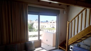 A room with a sofa, a wooden staircase, and a view of the outside. - Maria Apartments (Malevizi)