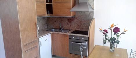 A compact kitchen with wooden cabinets, a built-in oven, a sink, and a dining table with chairs.