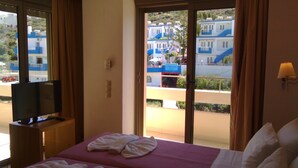 A hotel room with a bed, a television, and a view of buildings through the window. - Maria Apartments (Malevizi)
