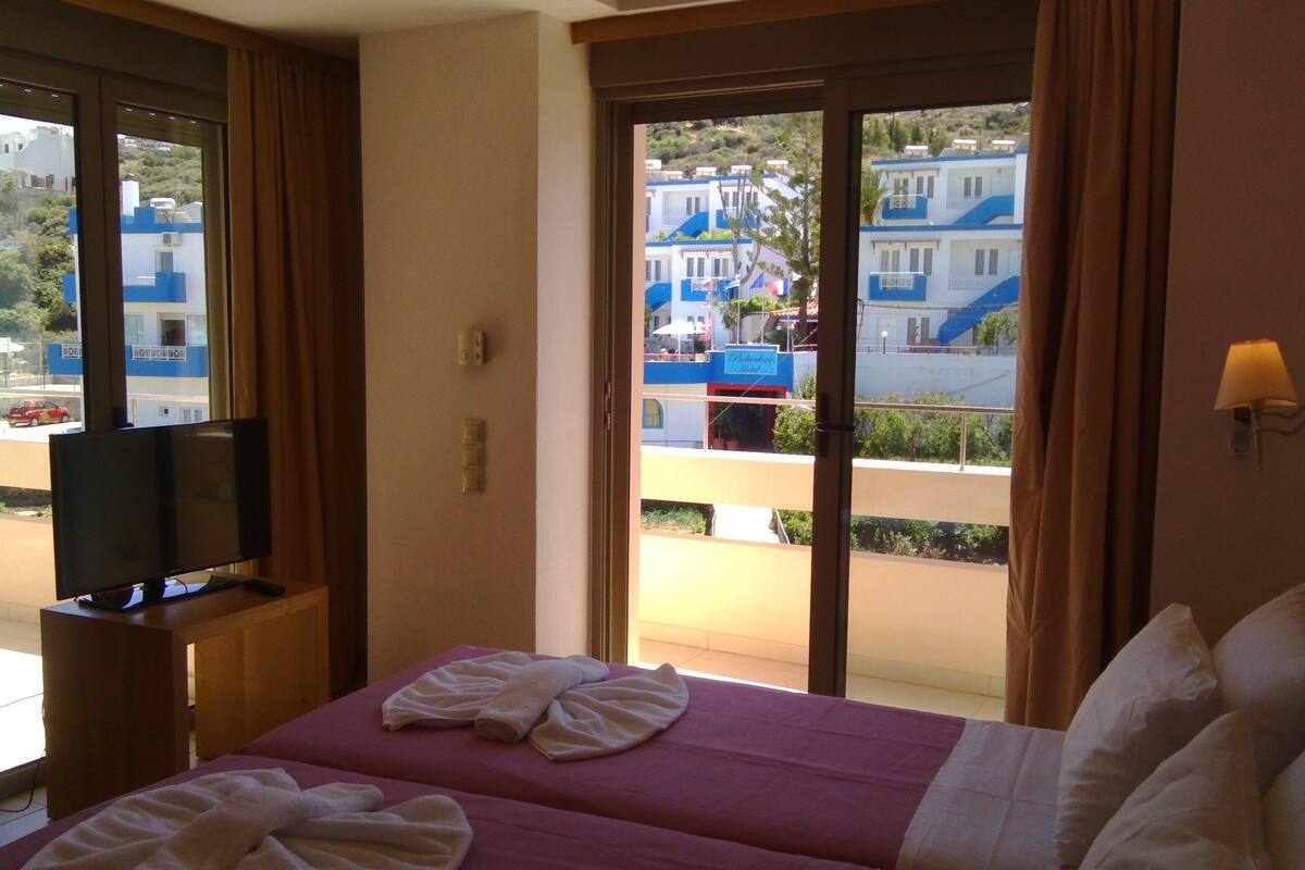 A hotel room with a bed, a television, and a view of buildings through the window.