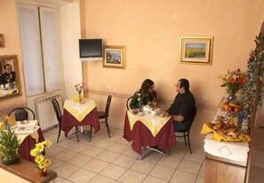 A dining area with two tables, each covered with a yellow and maroon tablecloth. There are chairs around the tables, and a buffet table with various food items is visible. - Arco Hotel (Milan)