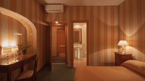 A hotel room with a bed, a desk with a lamp, a chair, a bathroom with a sink and mirror, and a door leading to another room. - Orange Garden Bed & Breakfast (Rome)