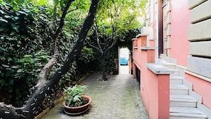 A narrow brick pathway flanked by lush greenery and a pink building with a staircase. - Orange Garden Bed & Breakfast (Rome)