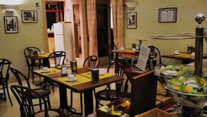 A dining area with tables and chairs, a buffet with food items, and a refrigerator in the background. - Hotel Dina (Rome)