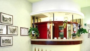 A reception area with a red leather couch, framed pictures on the wall, and a counter with a red door. - Hotel Dina (Rome)