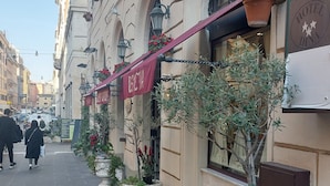 A street with a row of buildings, including a hotel with a sign that reads "HOTEL DINA". There are potted plants and a clear sky. - Hotel Dina (Rome)