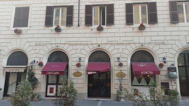 A building with multiple storefronts, including 'IL SECCJO', 'CAPITOLINA', and 'DEMETRA'. - Hotel Dina (Rome)
