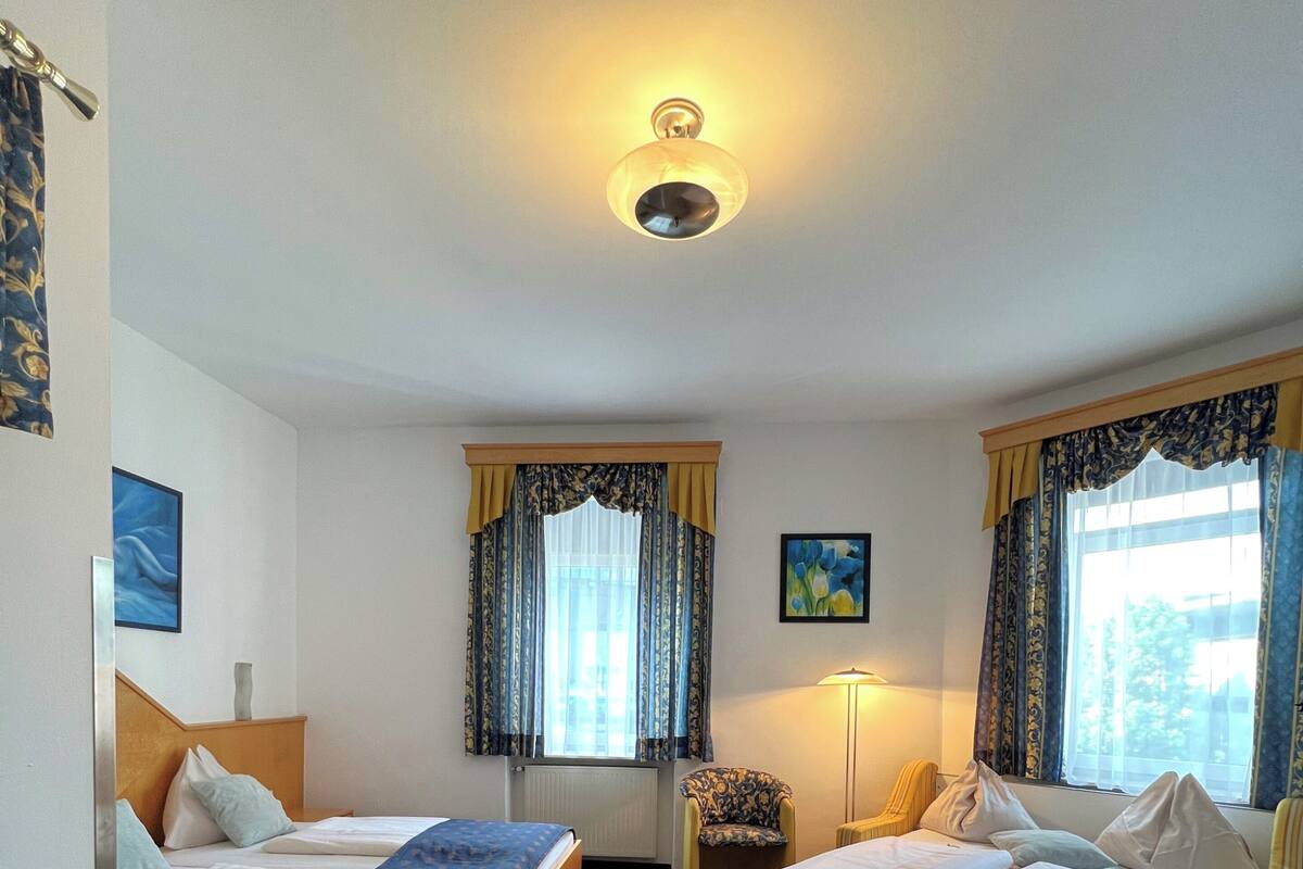 A hotel room with two beds, a desk, a chair, a lamp, and a painting on the wall.