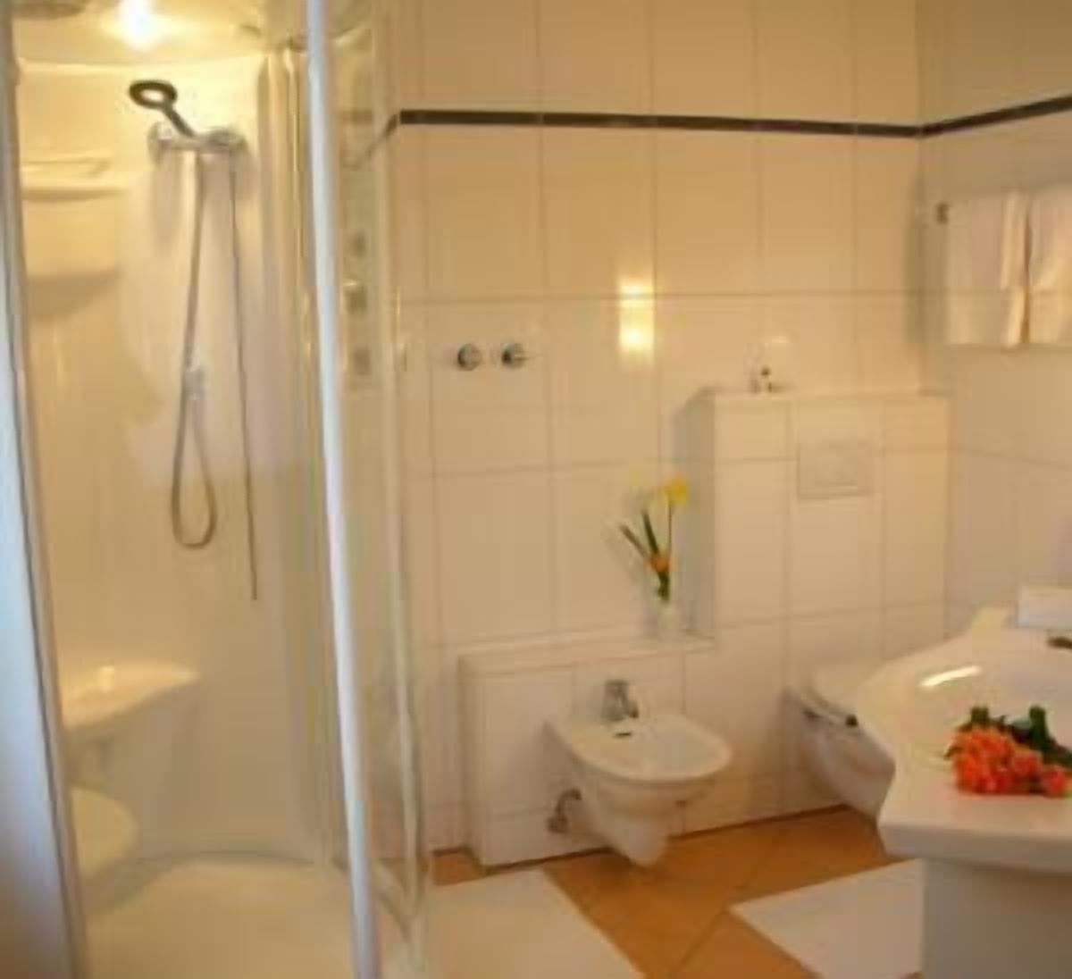 A bathroom with a glass-enclosed shower, a toilet, a bidet, and a sink with a vase of flowers.
