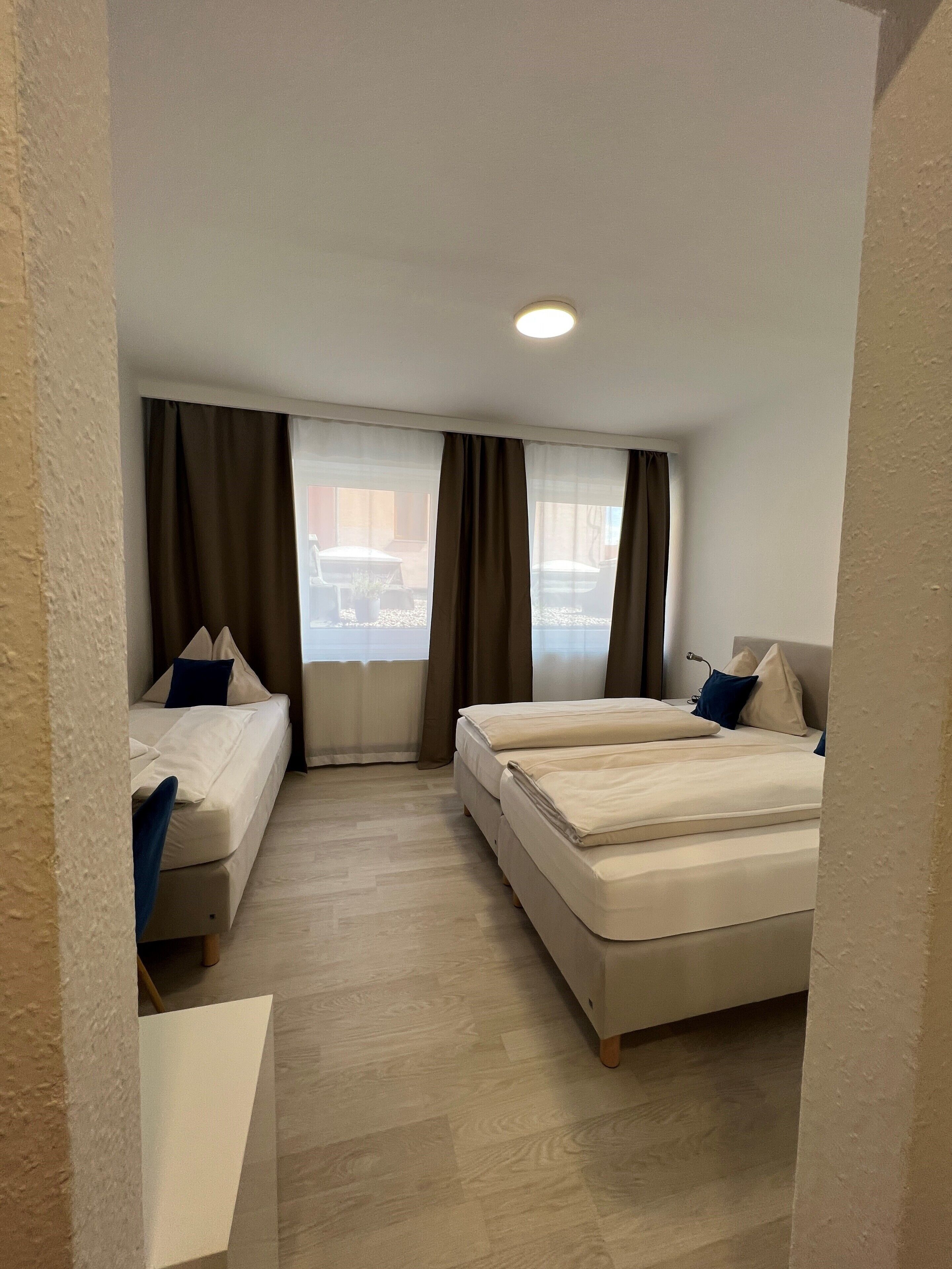 A hotel room with two beds, a sofa, and a large window with curtains.