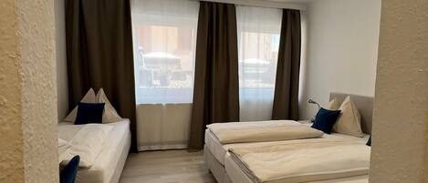 A hotel room with two beds, a sofa, and a large window with curtains.