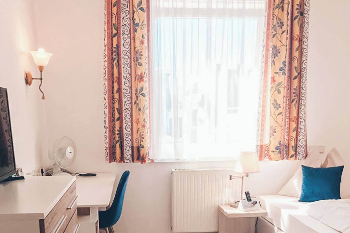 A room with a bed, a desk, a chair, a radiator, and curtains.