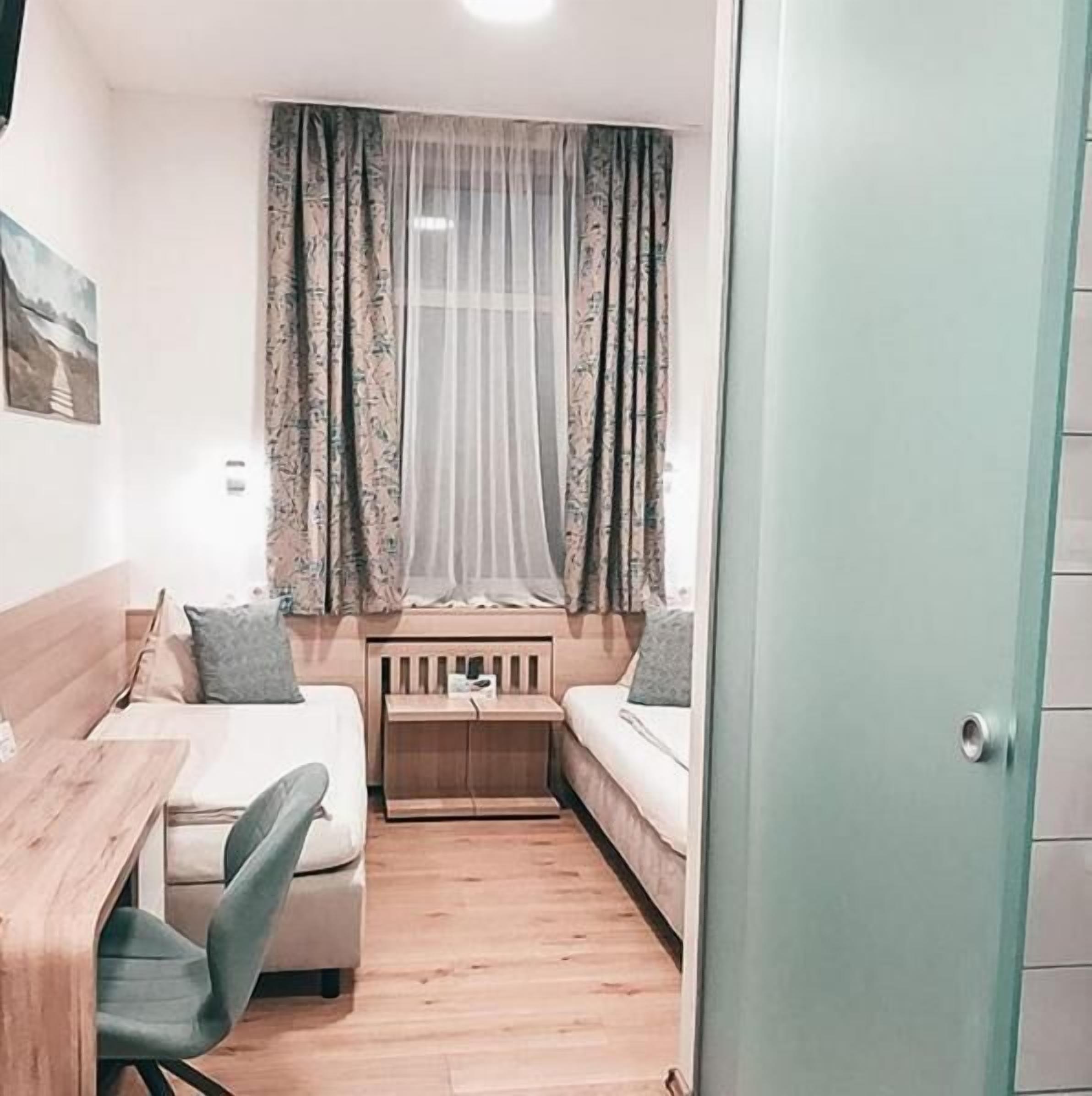 Une pièce de taille modeste, comprenant un bureau en bois, deux chaises, une petite table en bois et un canapé avec des coussins.
