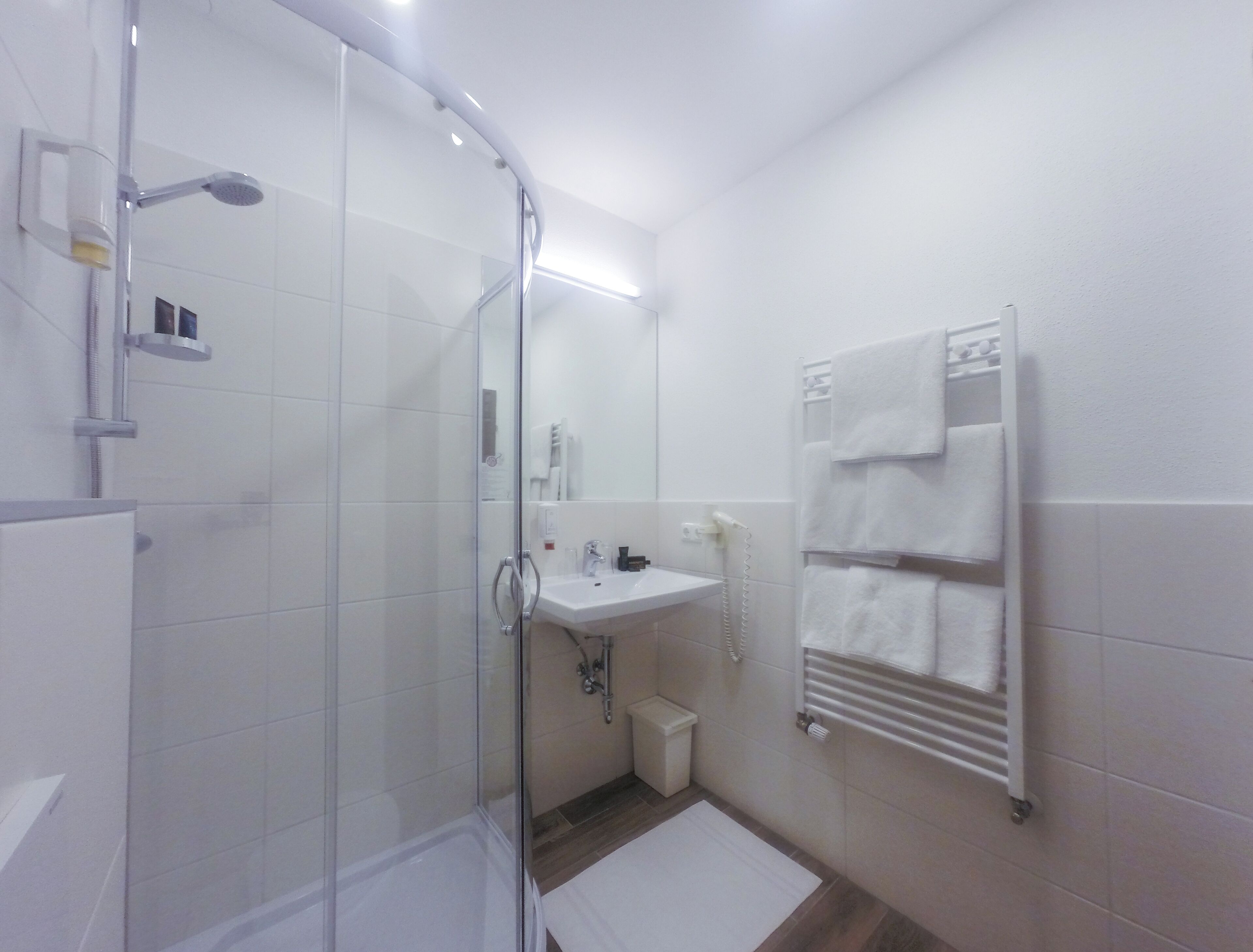 Un baño moderno con ducha de vidrio, un lavabo blanco y un perchero para toallas.