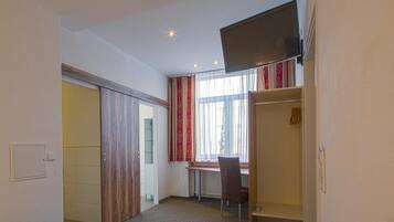 A hotel room with a bed, a desk, a chair, a wardrobe, and a television.