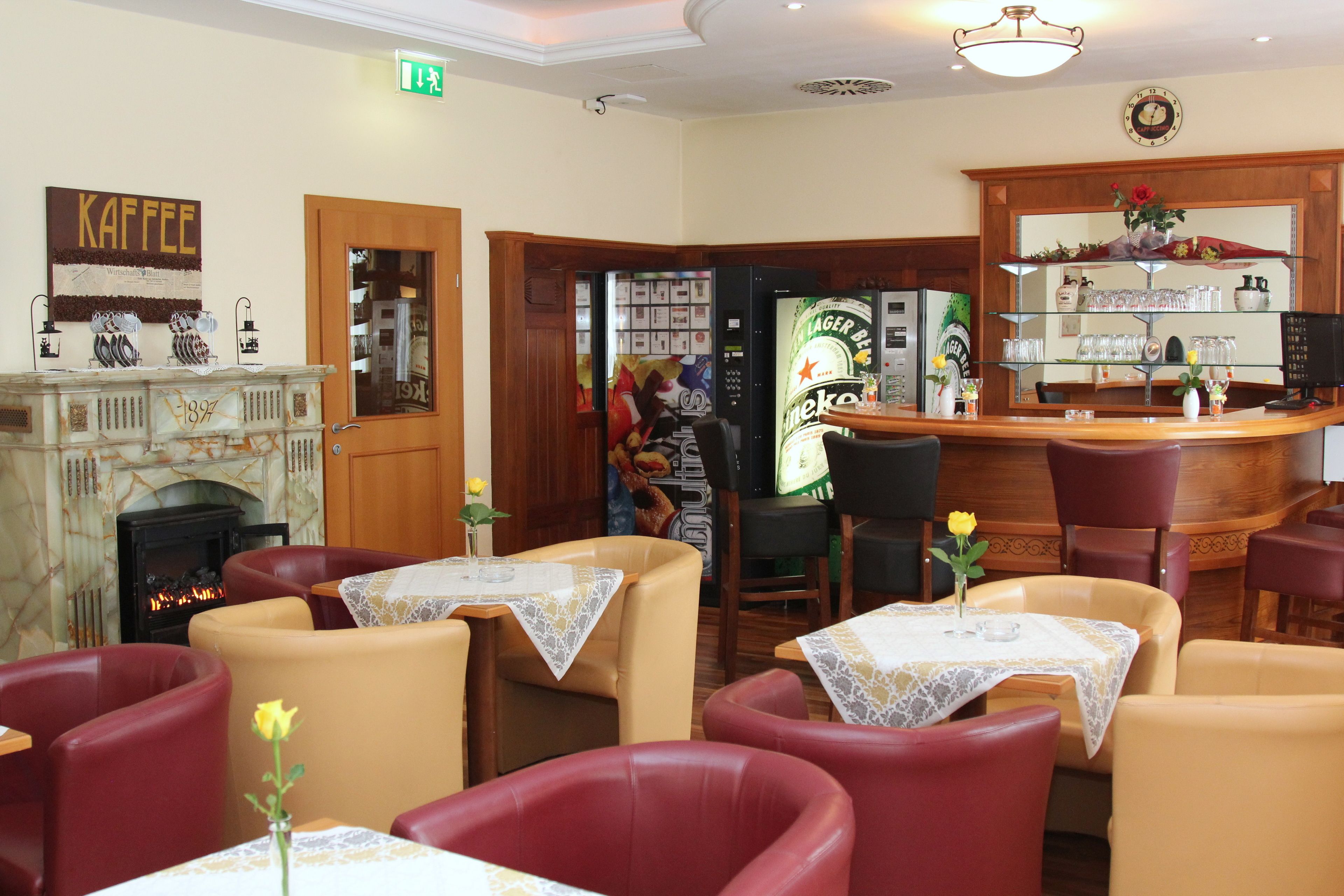 A cozy restaurant with leather chairs, tables with lace tablecloths, a fireplace, and a bar area with a beer dispenser.