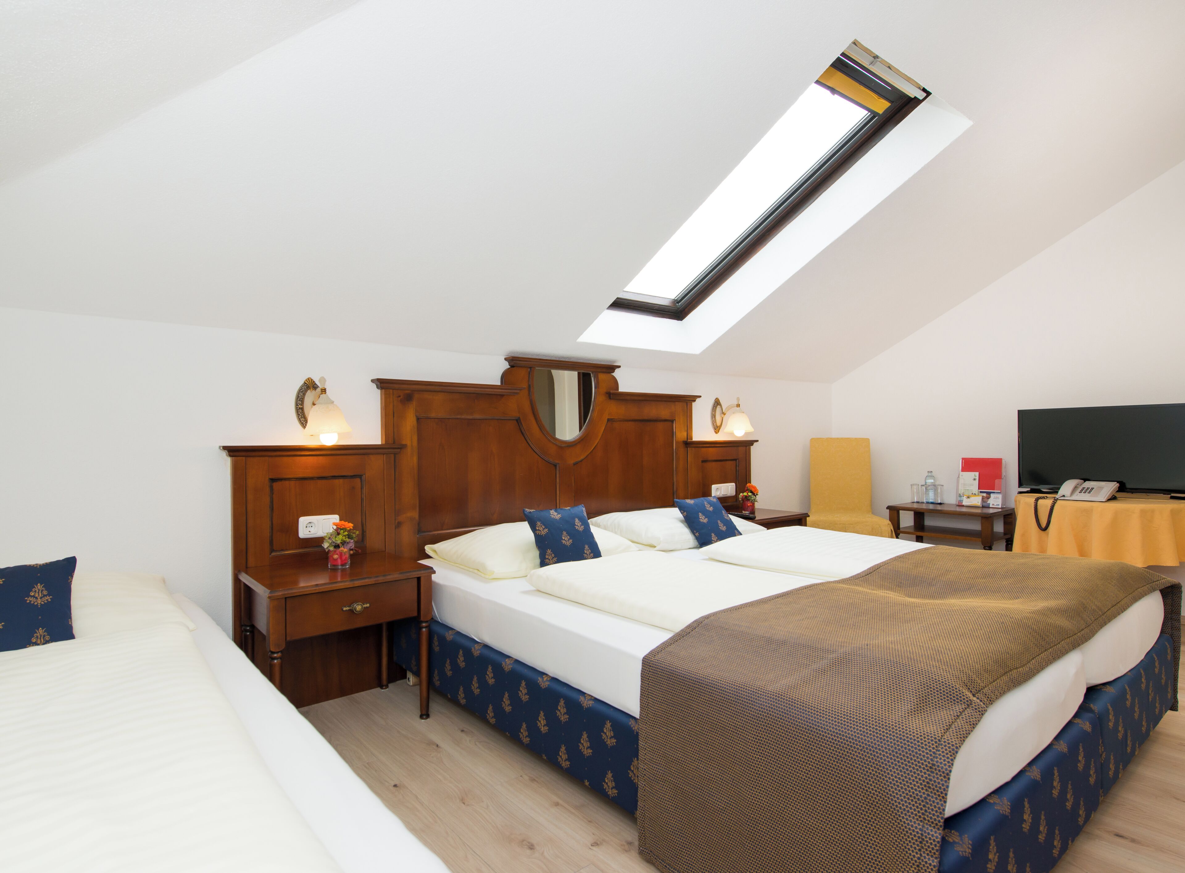Une chambre d’hôtel avec une lucarne, un lit, une table de chevet, une chaise et un bureau avec un téléphone.