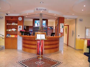 Un área de recepción con un mostrador de madera curvado, un reloj y un cartel de recepción.