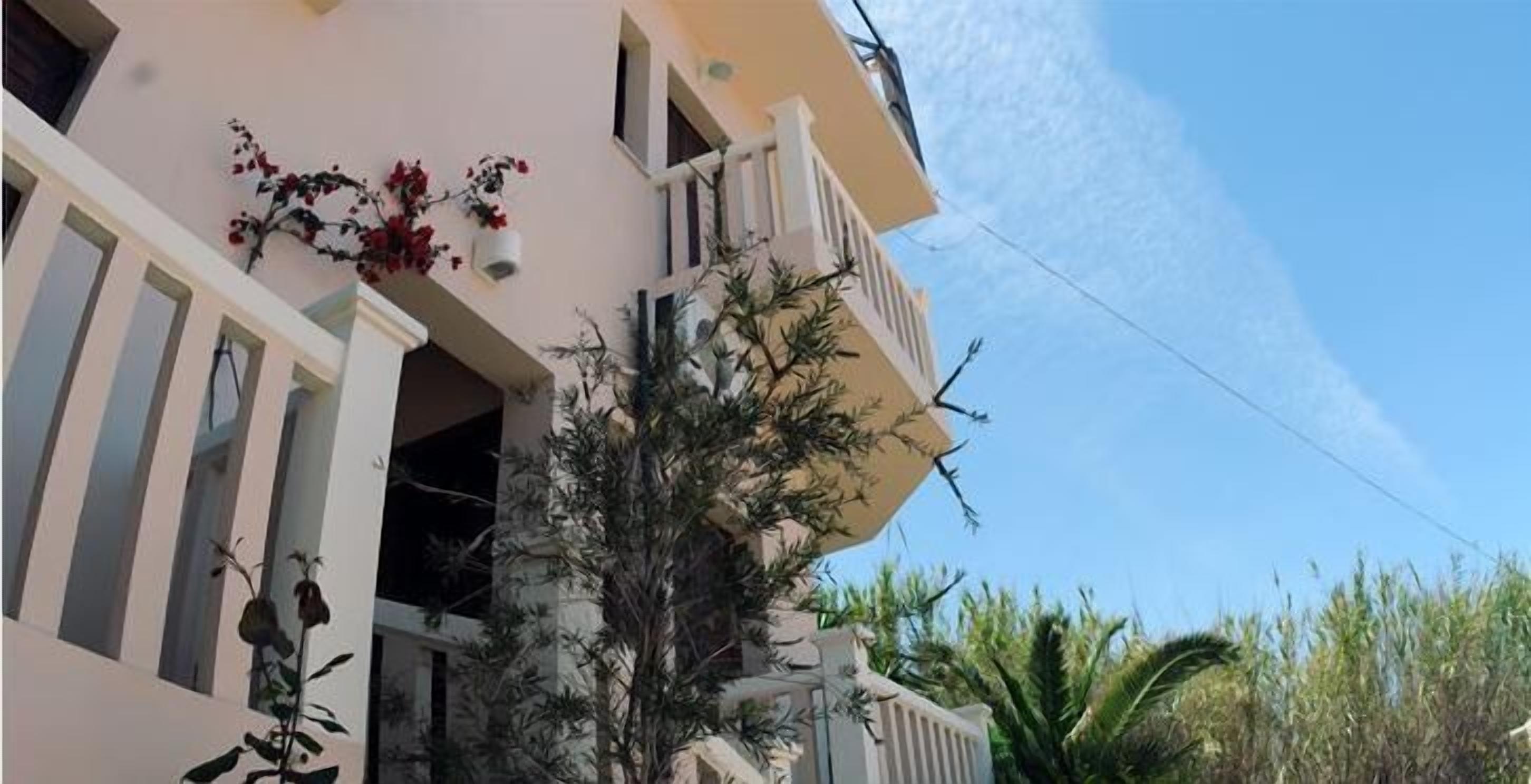 A multi-story building with balconies, large windows, and some greenery.
