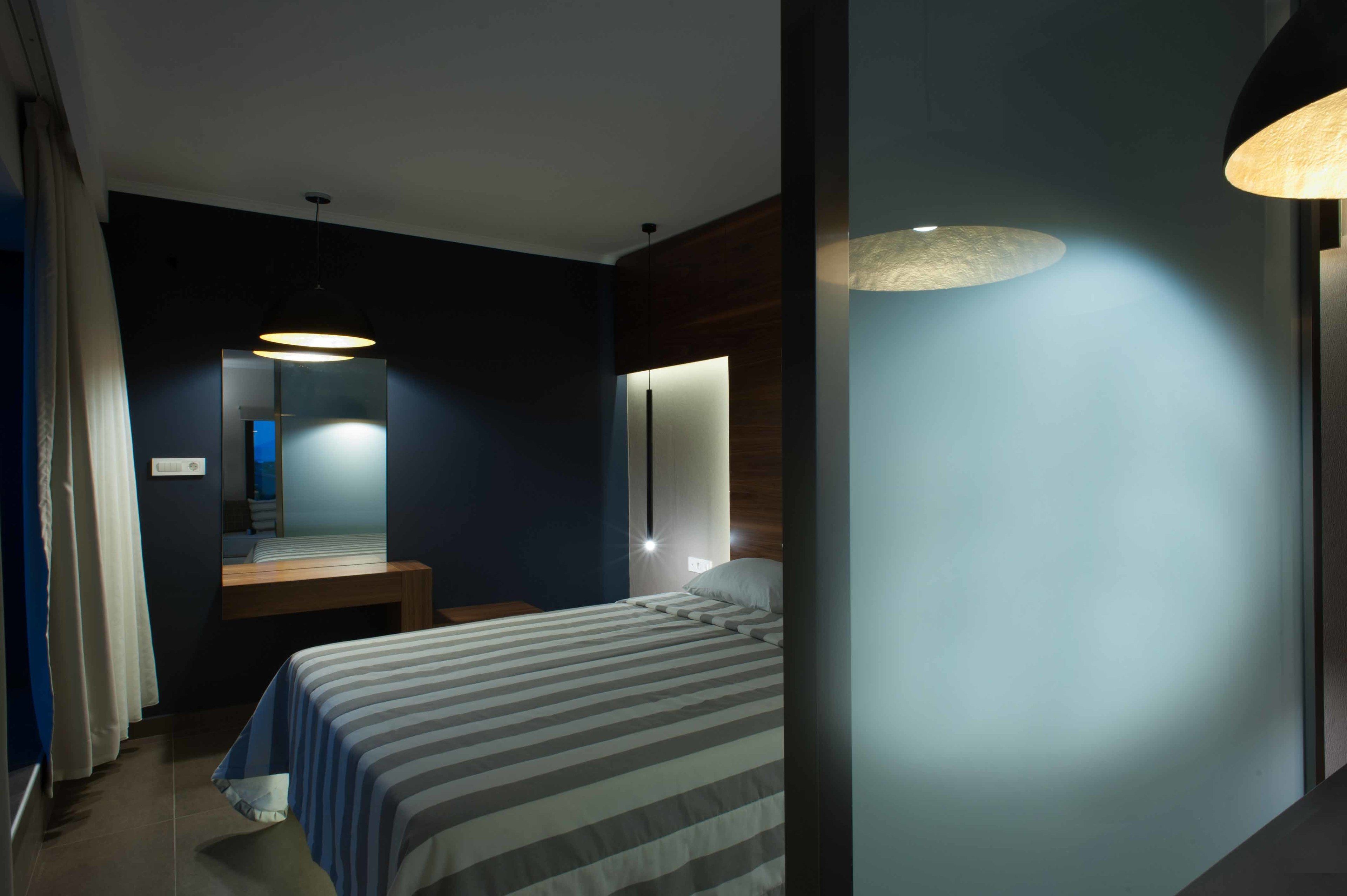 A modern hotel room with a bed, bedside table, and a mirror.