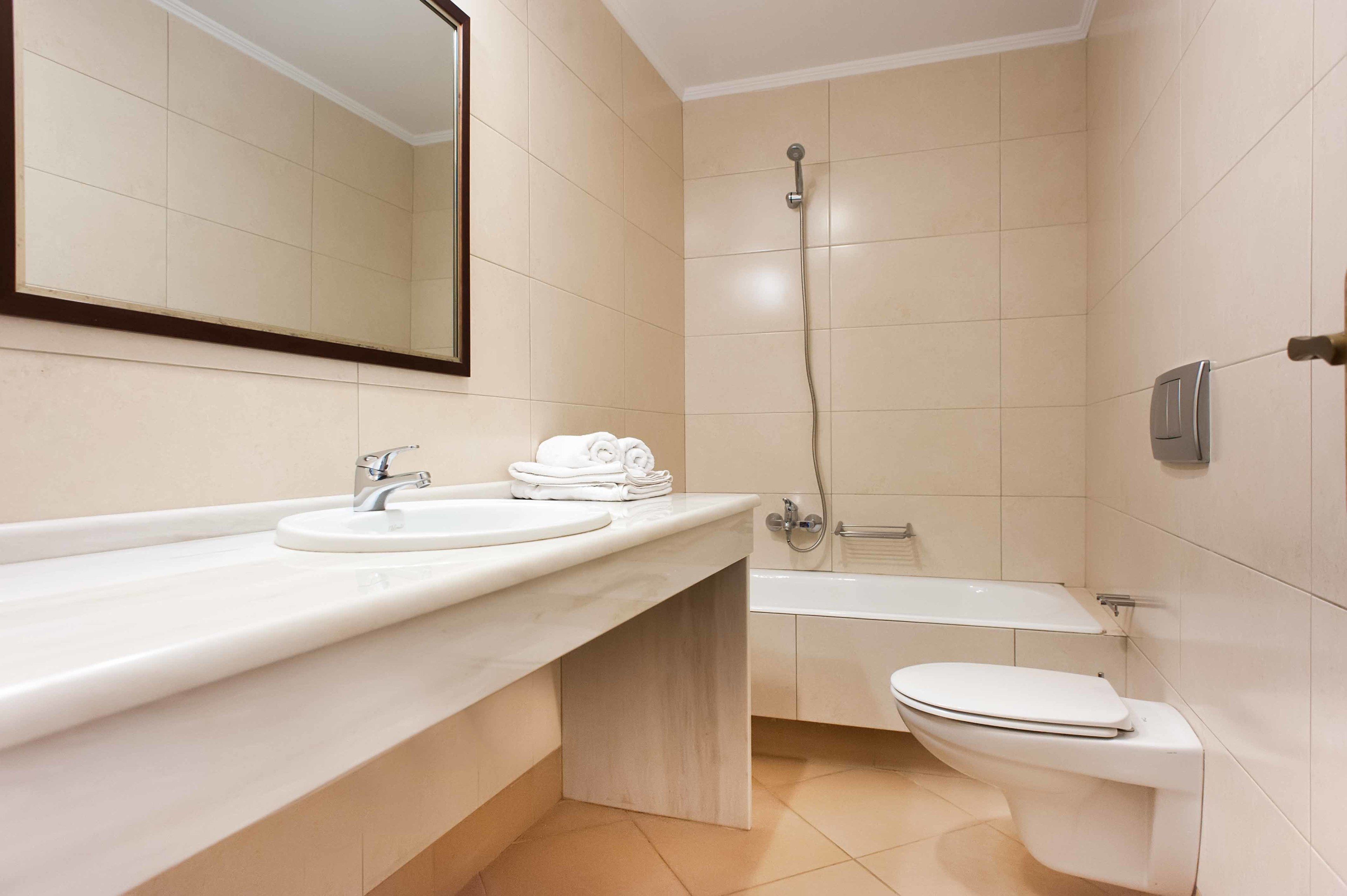 A modern bathroom with a sink, mirror, toilet, and shower.