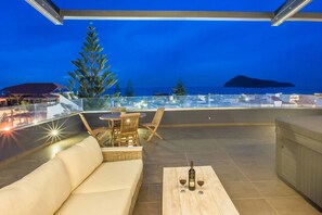 A rooftop terrace with a sofa, chairs, and a table with a bottle and glasses.