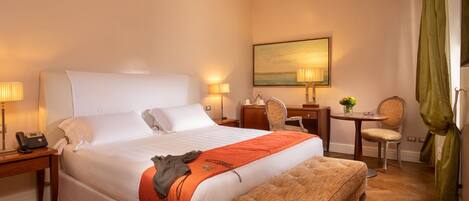 A hotel room with a large bed, a bedside table with a lamp, a small desk with a chair, and a painting on the wall.
