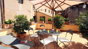 An outdoor patio with a table and chairs, surrounded by potted plants and a large umbrella. - Vivaldi Luxury Rooms (Rome)