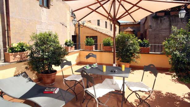 An outdoor patio with a table and chairs, surrounded by potted plants and a large umbrella. - Vivaldi Luxury Rooms (Rome)
