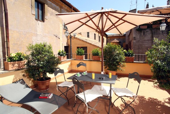 An outdoor patio with a table and chairs, surrounded by potted plants and a large umbrella. - Vivaldi Luxury Rooms (Rome)