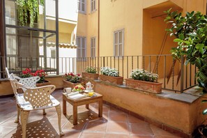 A sunlit outdoor seating area with a table, chairs, and potted plants. - Vivaldi Luxury Rooms (Rome)