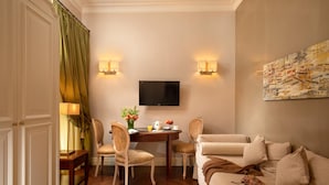 A hotel room with a dining area, a TV mounted on the wall, and a painting on the wall. - Vivaldi Luxury Rooms (Rome)