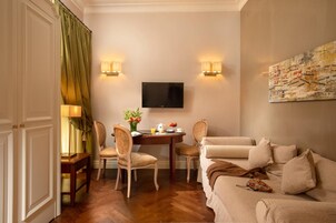 Habitación de hotel con zona de comedor, televisor montado en la pared y un cuadro.