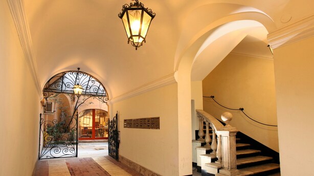 A grand hallway with an arched entrance, a staircase with balusters, and a decorative iron gate. - Vivaldi Luxury Rooms (Rome)