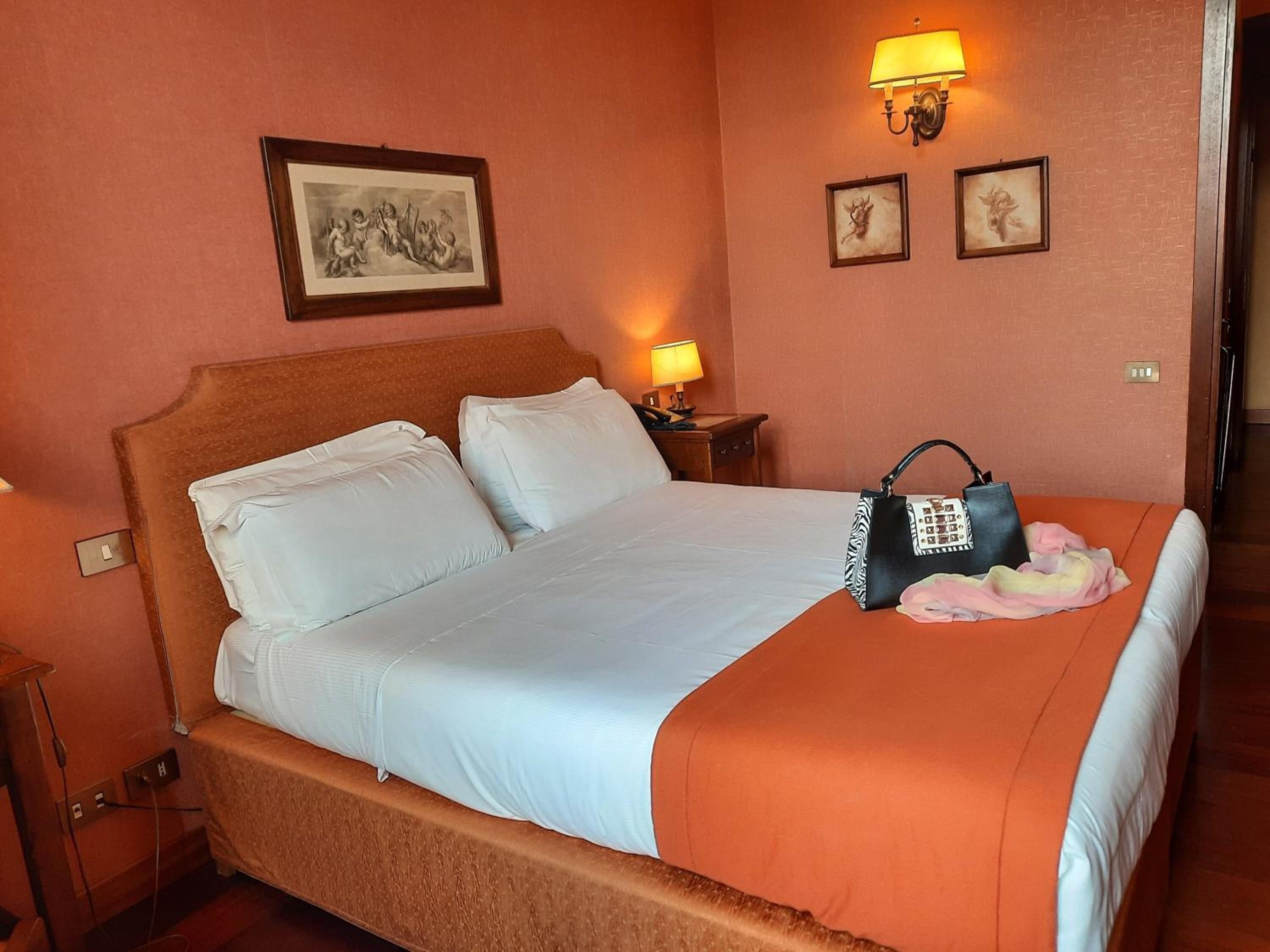A hotel room with a bed, a nightstand, and a lamp.
