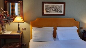 A hotel room with a bed, two bedside tables, a lamp, a framed picture on the wall, and a vase with plants. - Domus Livia Luxury Suites (Rome)