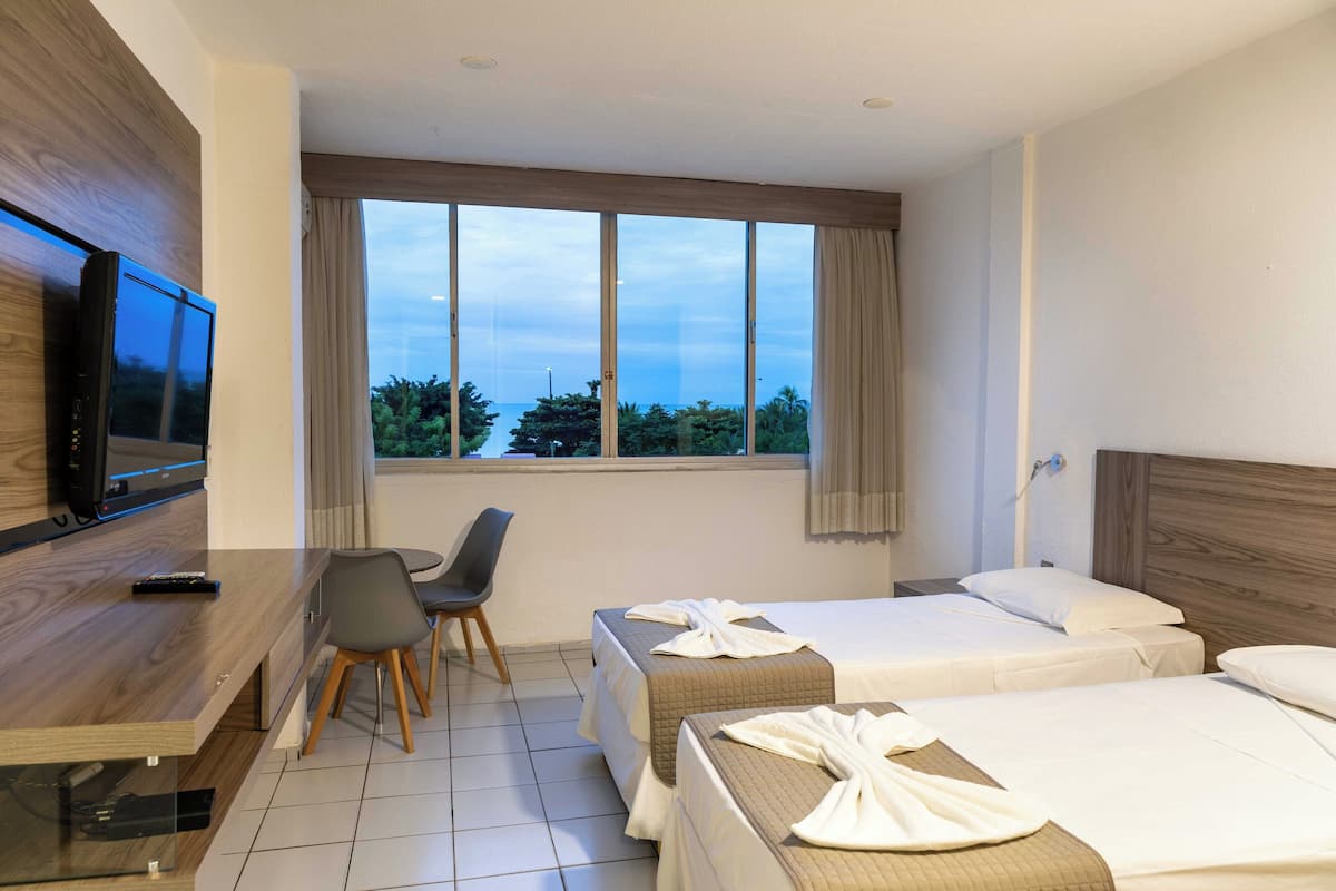 Une chambre d’hôtel avec deux lits, un bureau avec une chaise, une télévision et une grande fenêtre avec des rideaux.
