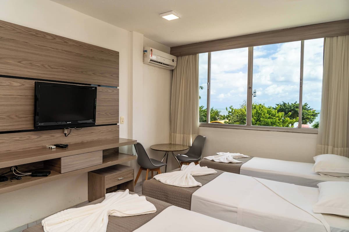 Une chambre d’hôtel avec deux lits, une télévision, une table avec des chaises et une fenêtre donnant sur un paysage verdoyant.